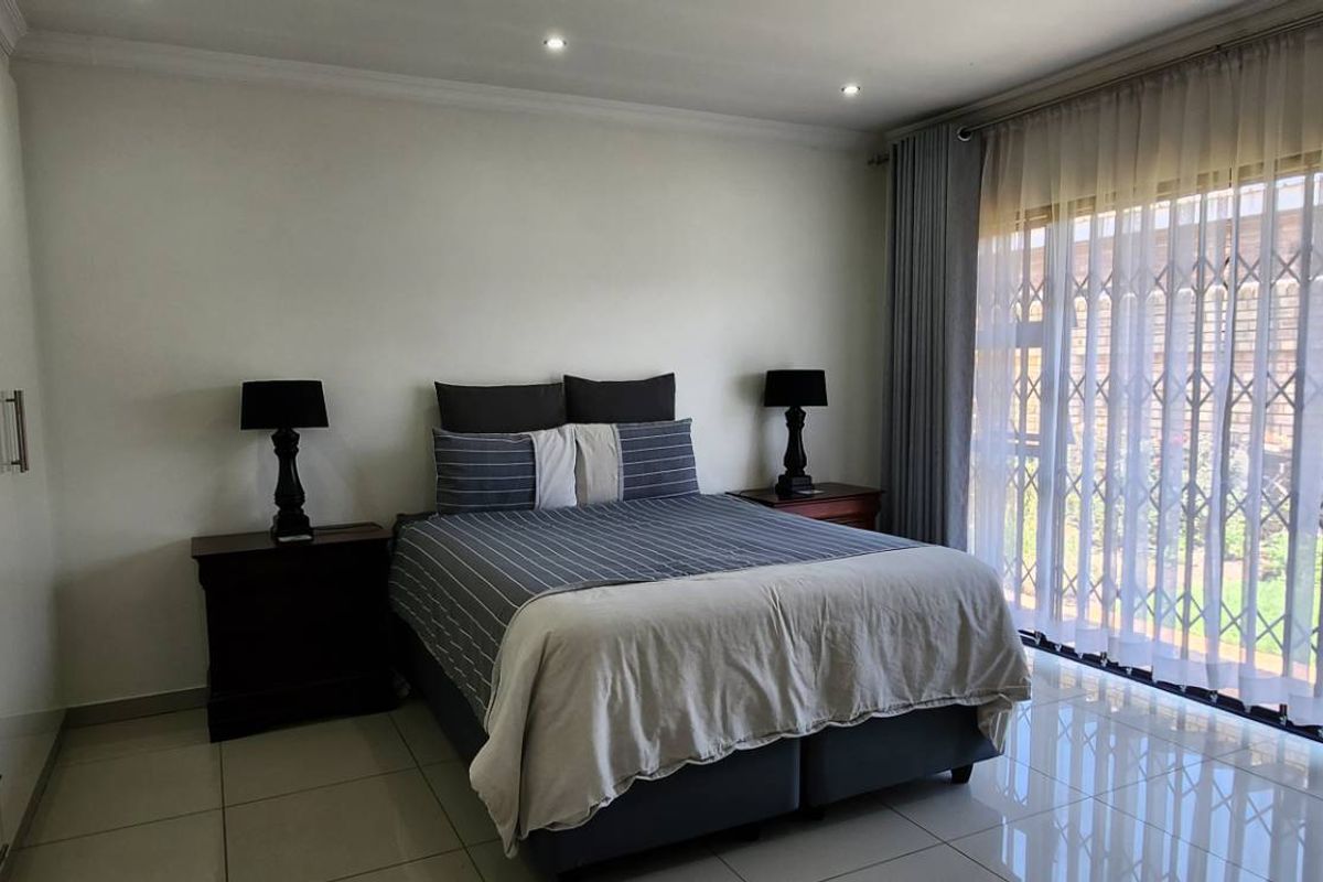 Spacious bedroom featuring high-gloss built-in cupboards, tiled flooring, and large sliding doors with security gates leading to the garden.