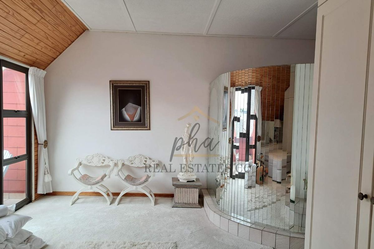A bedroom featuring a curved mirrored wall, wood-paneled ceiling accents, and large windows providing natural light.