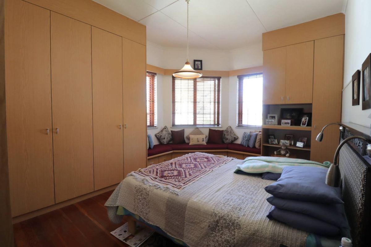 A well-maintained bedroom featuring extensive built-in cabinetry, timber flooring, and a cozy bay window with a built-in seating area.