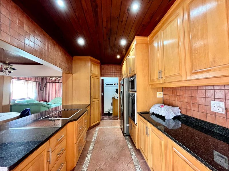 A functional kitchen featuring wooden cabinetry, granite countertops, built-in appliances, and a distinctive wooden paneled ceiling with recessed lighting.