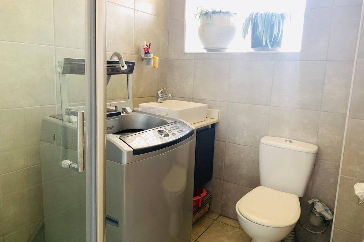 Compact bathroom featuring a shower enclosure, toilet, and vanity basin with neutral wall and floor tiling.