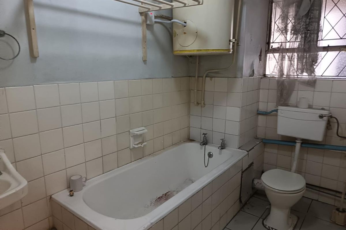 A dated bathroom featuring a bathtub, toilet, and wall-mounted water heater, requiring significant renovation and cosmetic updates to improve its condition.