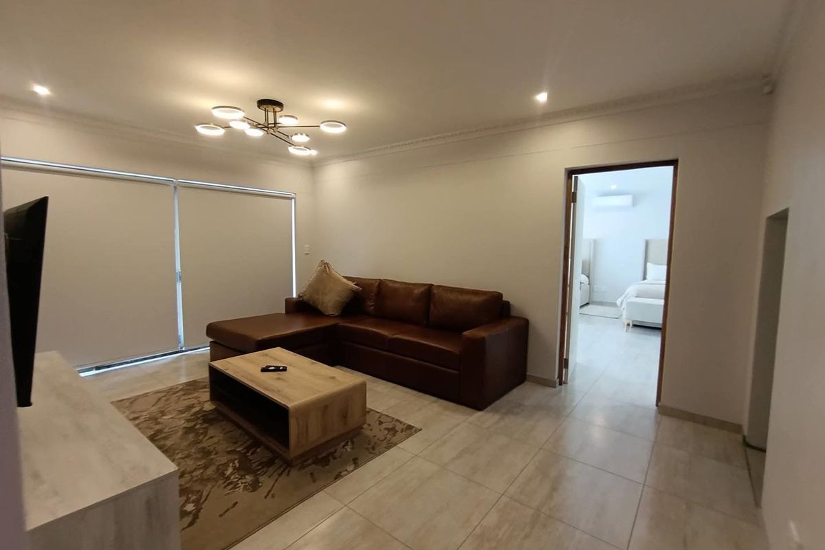 A bright and modern living room featuring large format floor tiles, recessed downlighting, a contemporary chandelier, and sliding glass doors with roller blinds.