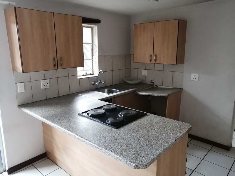 A functional kitchen featuring laminate cabinetry, a built-in electric hob, stainless steel sink, and tiled backsplash with neutral ceramic flooring.