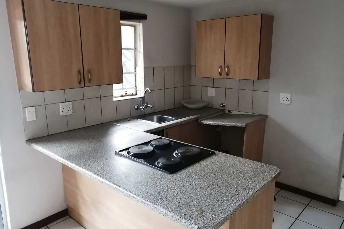 A functional kitchen featuring laminate cabinetry, a built-in electric hob, stainless steel sink, and tiled backsplash with neutral ceramic flooring.