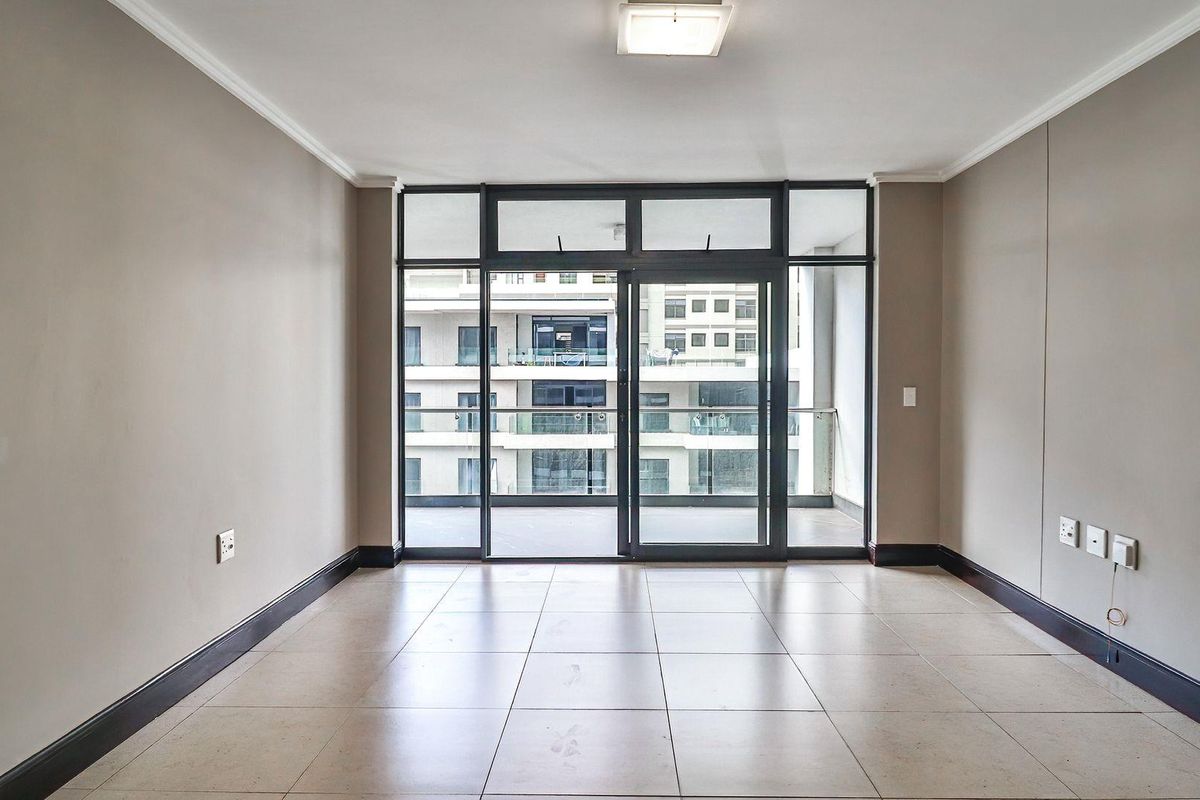 A bright, empty living area featuring neutral tiled flooring, dark skirting boards, and large sliding glass doors leading to an outdoor balcony.