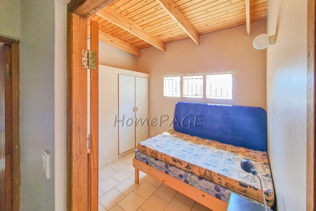 A compact bedroom featuring a timber-clad vaulted ceiling, tiled flooring, and a built-in wardrobe.