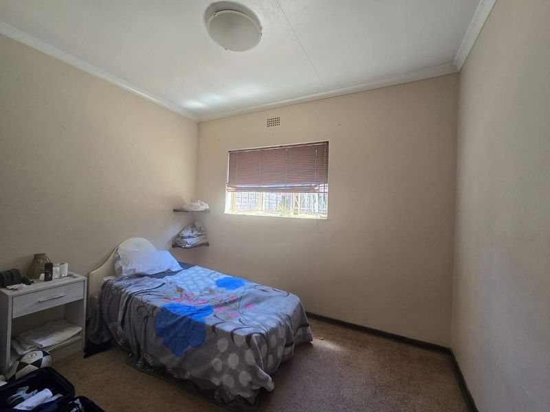 A compact bedroom featuring carpeted flooring, a window with venetian blinds, and built-in corner shelving.