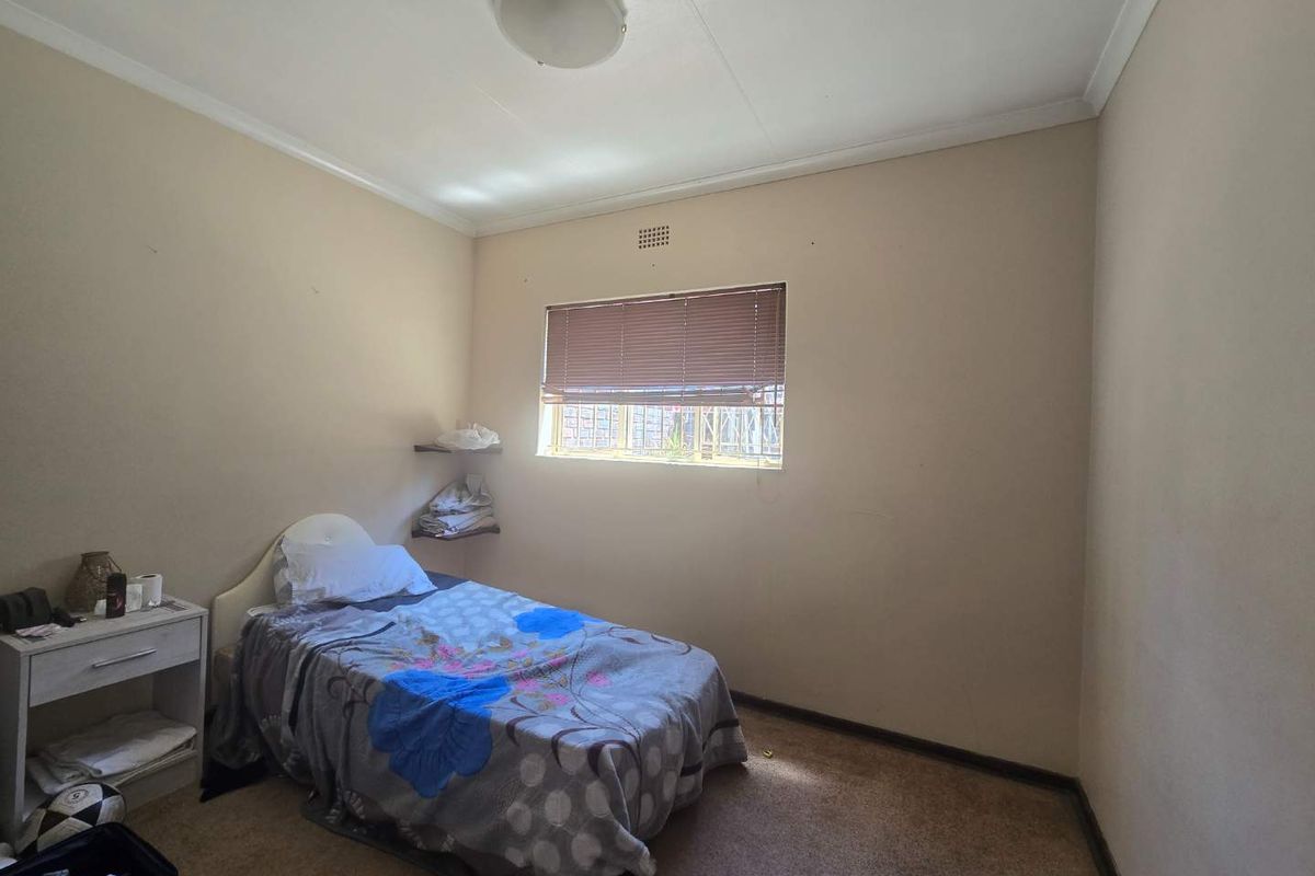 A compact bedroom featuring carpeted flooring, a window with venetian blinds, and built-in corner shelving.