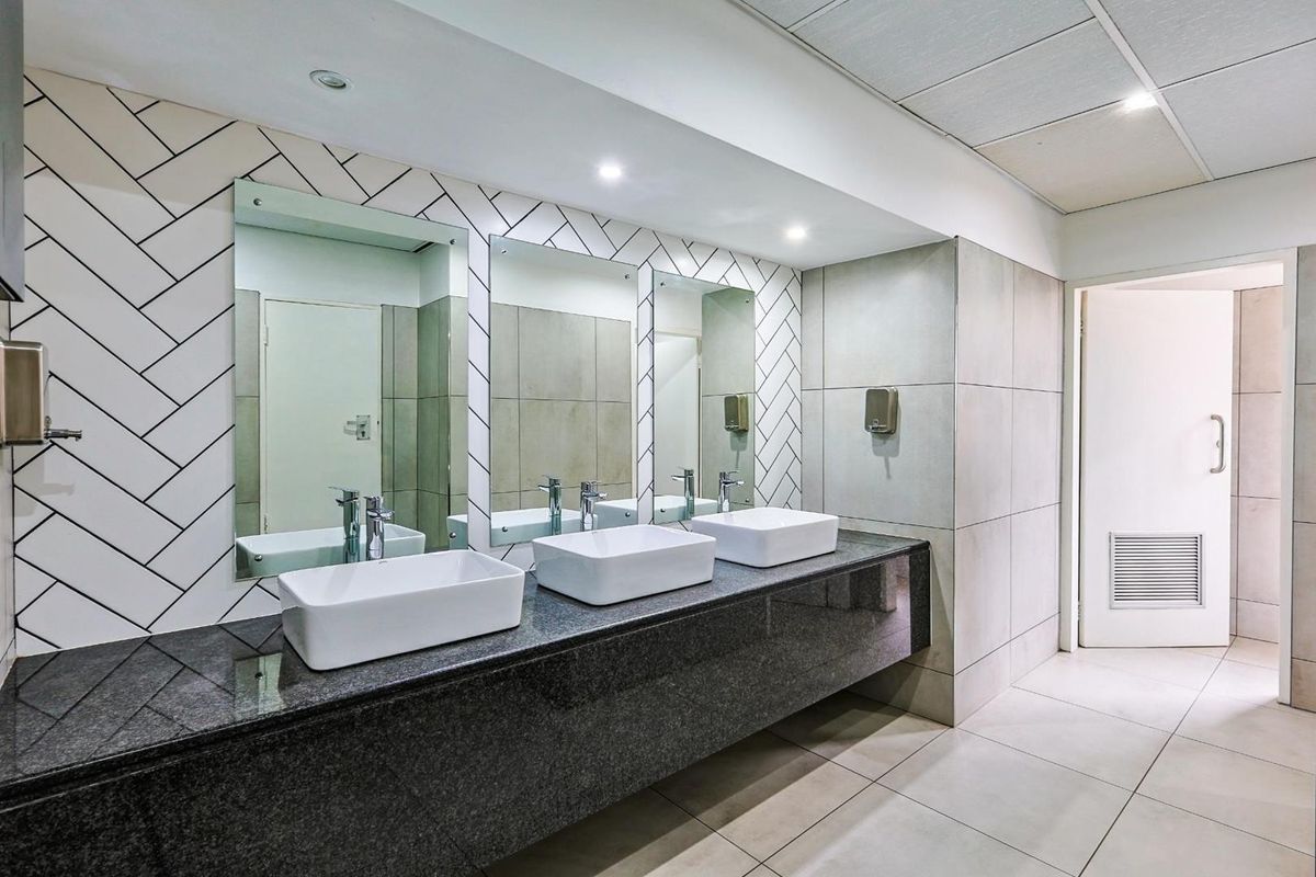 A modern commercial bathroom featuring a triple vanity with vessel sinks, granite countertop, and stylish herringbone-patterned wall tiling.