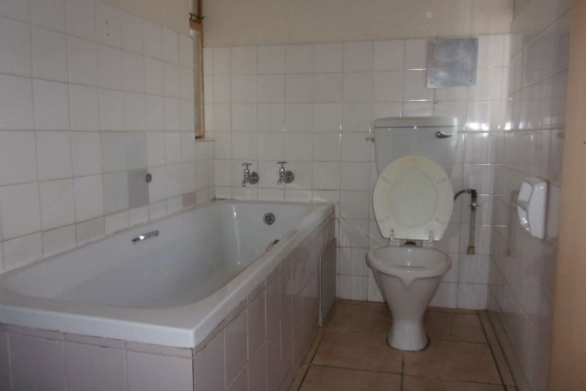 A dated bathroom featuring a built-in bathtub and a standard toilet, finished with white wall tiles and tiled flooring.