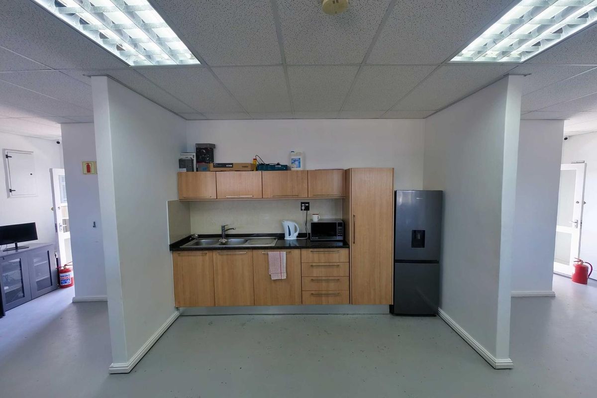 A compact office kitchenette featuring light wood cabinetry, a stainless steel sink, and a dark countertop, set within a dedicated alcove.
