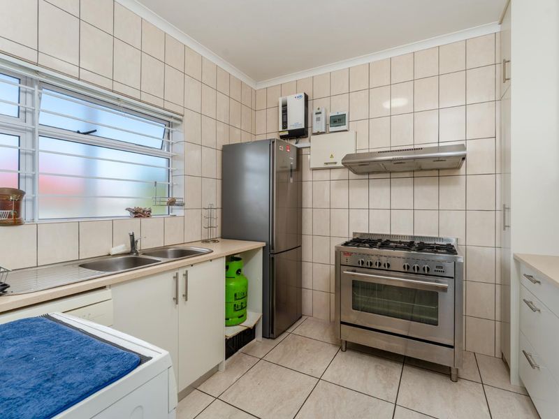 Functional kitchen featuring tiled walls and flooring, stainless steel double sink, gas stove with extractor fan, and ample built-in cabinetry.