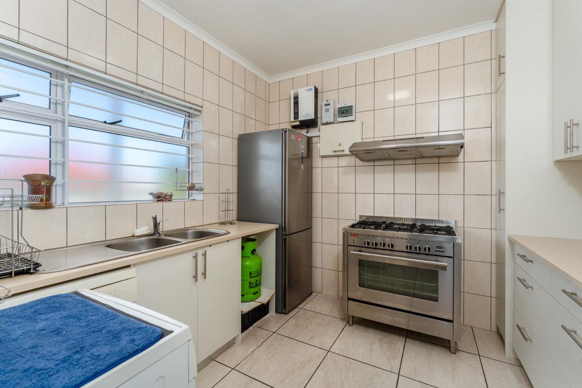 Functional kitchen featuring tiled walls and flooring, stainless steel double sink, gas stove with extractor fan, and ample built-in cabinetry.