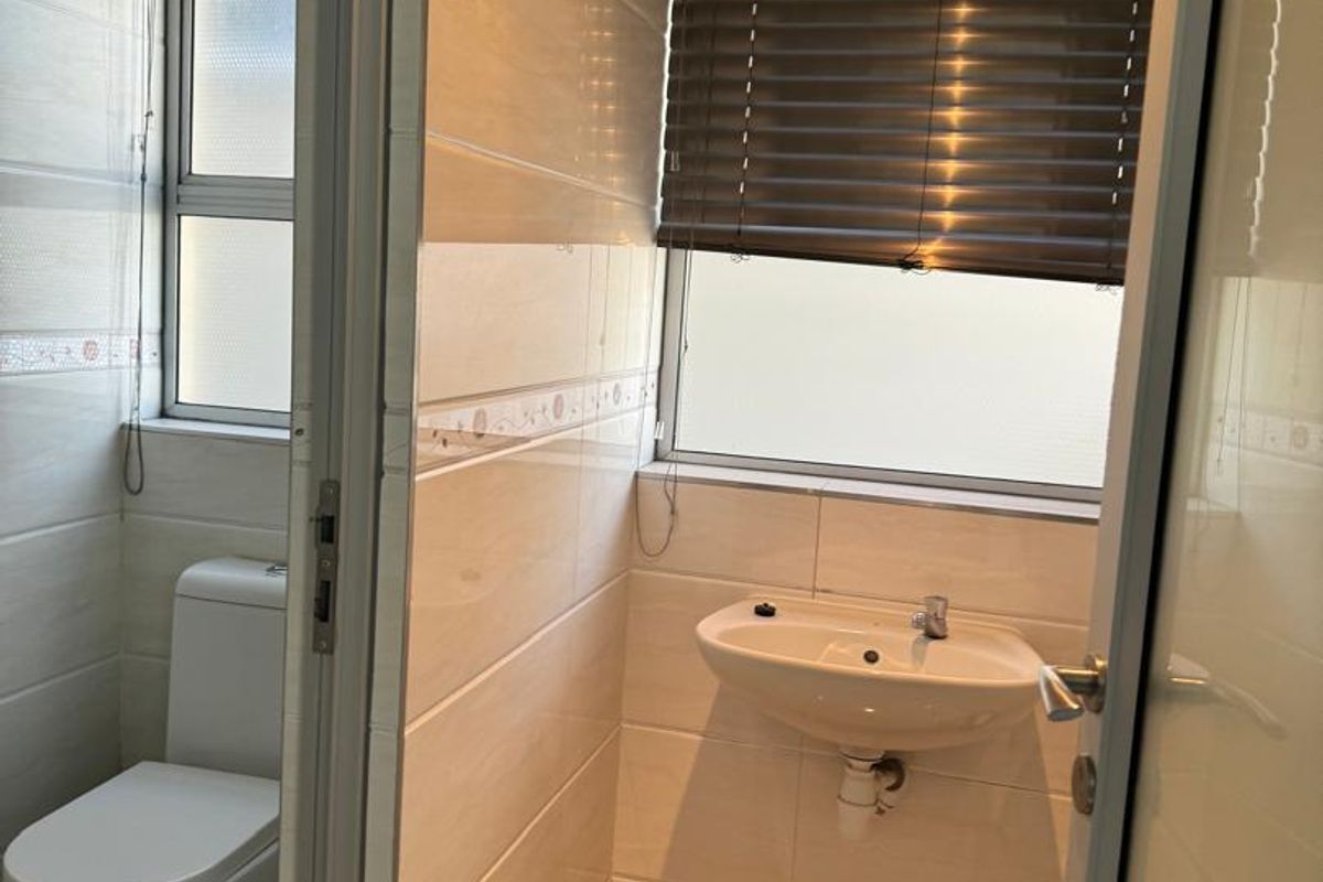 A functional office restroom featuring a wall-mounted basin and a separate toilet cubicle with tiled walls and flooring.