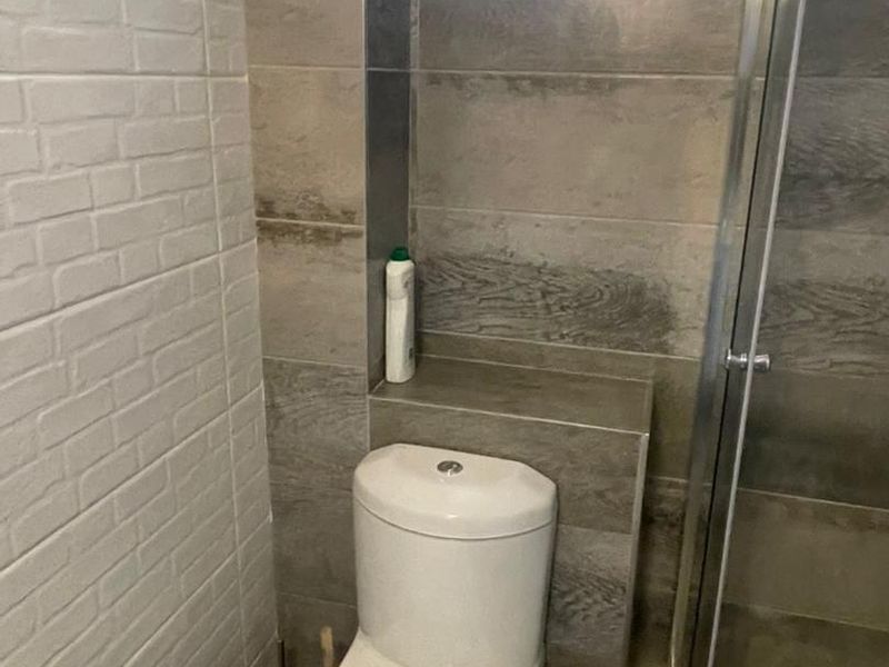 A modern bathroom featuring a toilet, a glass-enclosed shower, and contemporary grey tiled walls with a built-in tiled storage shelf.