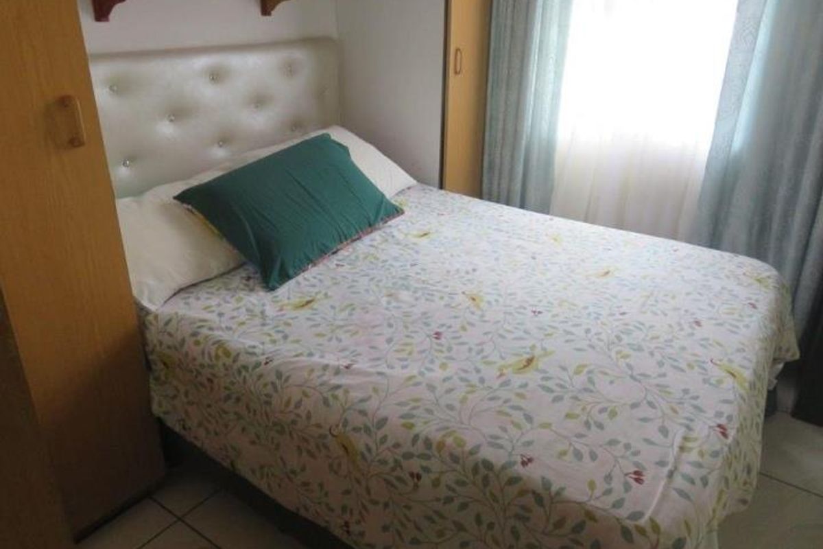 A compact bedroom featuring built-in cupboards, tiled flooring, and a fitted headboard, providing a functional and organized sleeping space.