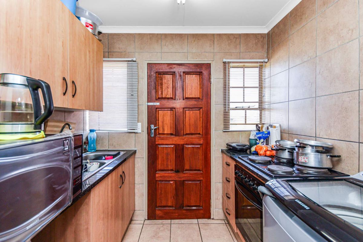 A compact kitchen featuring built-in cabinetry, granite countertops, a fitted oven and hob, and tiled wall finishes.