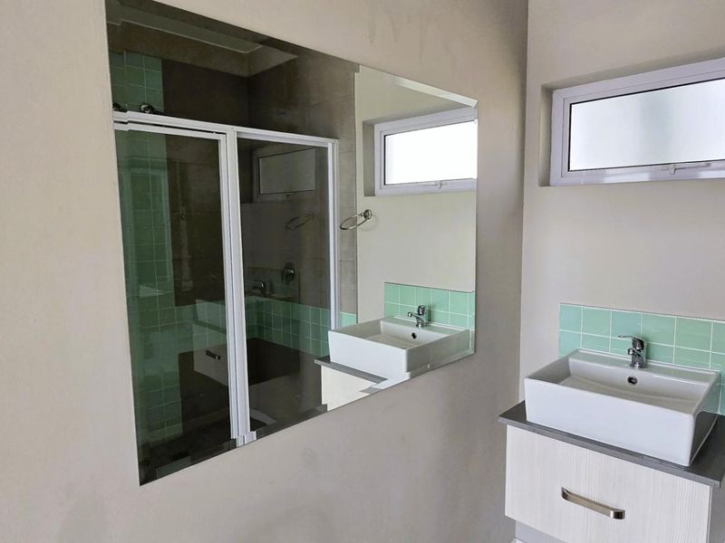 A clean, modern bathroom featuring a vessel sink on a vanity cabinet, a large wall mirror, and a tiled shower enclosure.