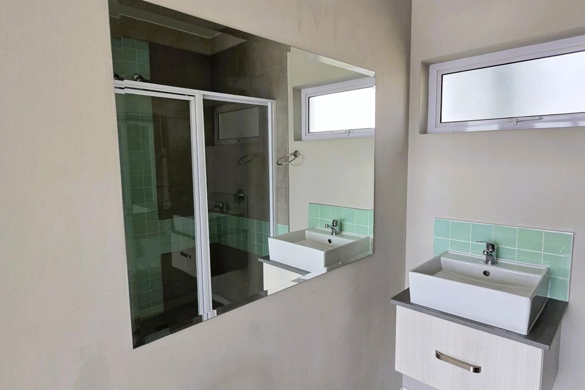 A clean, modern bathroom featuring a vessel sink on a vanity cabinet, a large wall mirror, and a tiled shower enclosure.