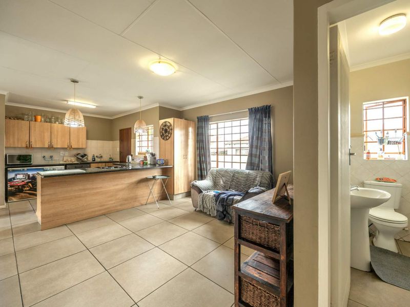 Open-plan kitchen and living area featuring tiled floors, wooden cabinetry, and granite countertops, with an adjacent bathroom visible through the doorway.