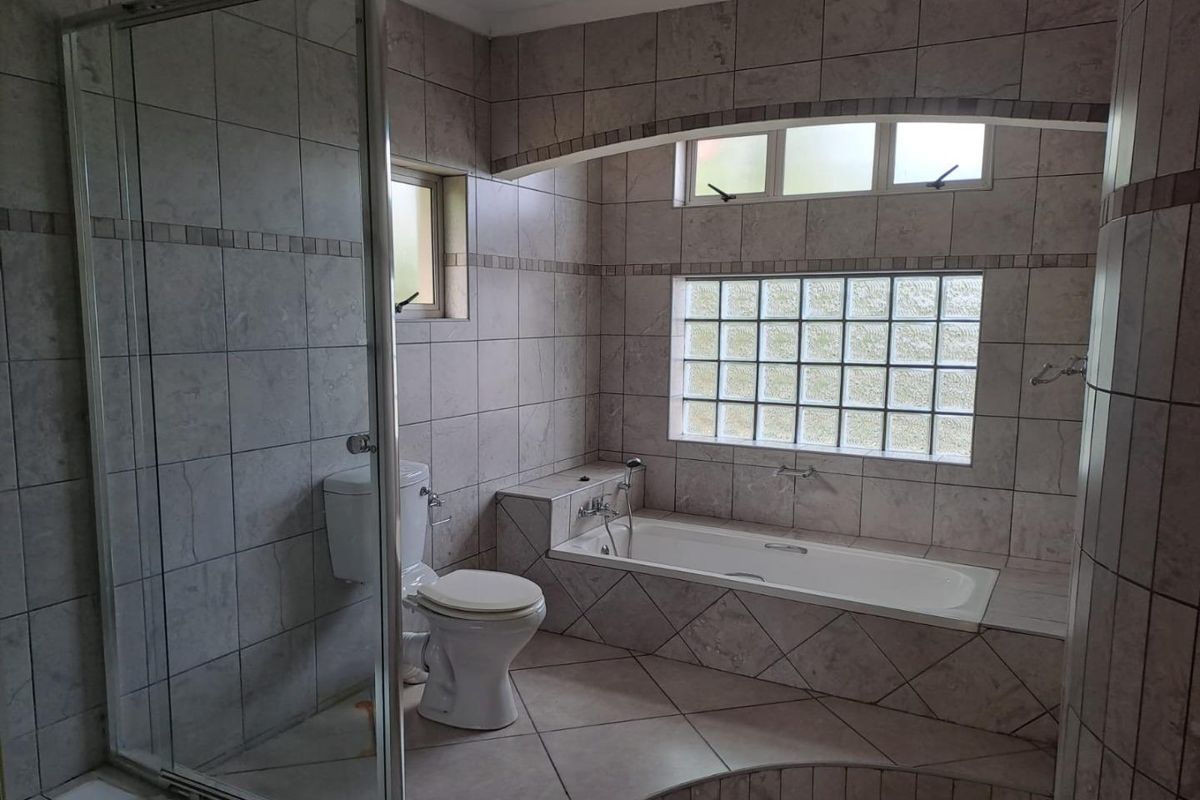 A spacious bathroom featuring a built-in bathtub, a separate glass-enclosed shower, and neutral wall and floor tiling with a decorative glass block window.