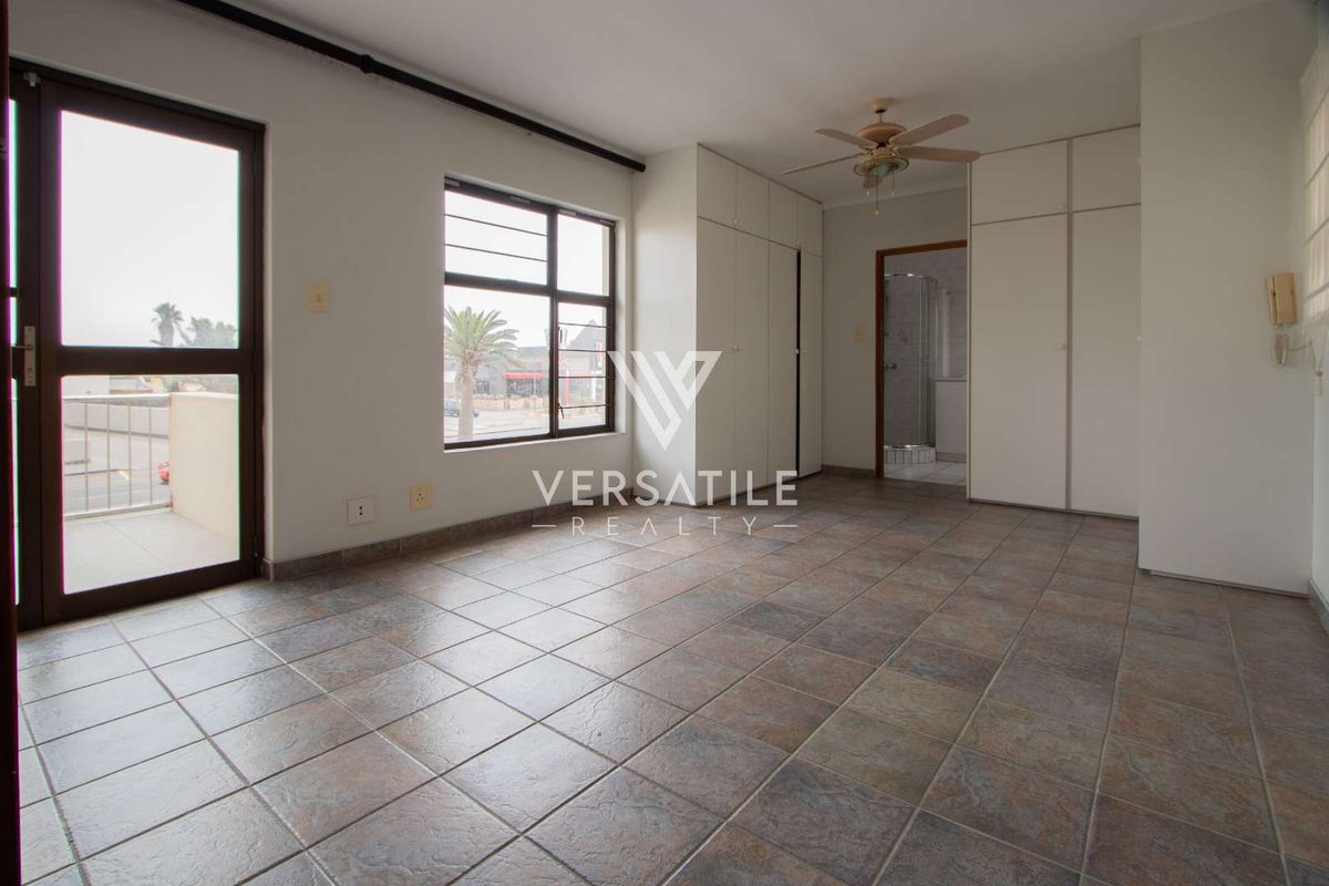 A spacious bedroom featuring tiled flooring, built-in cupboards, a ceiling fan, and direct access to a private balcony.