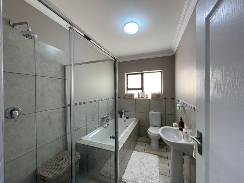 A functional bathroom featuring a glass-enclosed shower, a built-in bathtub, a pedestal sink, and a toilet with neutral wall and floor tiling.