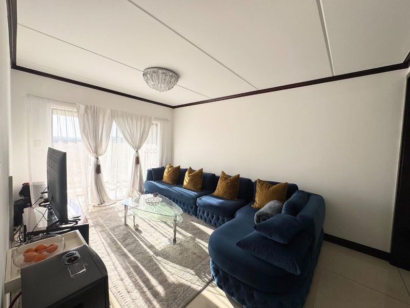 A bright living room featuring tiled flooring, a central ceiling light fixture, and a sliding glass door providing access to the exterior.