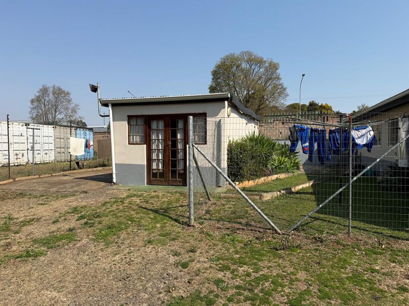 Rear view of a detached outbuilding featuring timber-framed glass doors, set within a fenced yard area with a concrete apron.