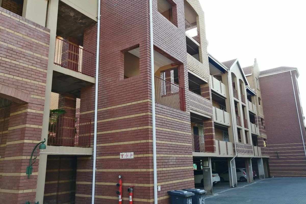 Exterior view of a multi-story apartment complex featuring face brick construction, private balconies, and ground-level covered parking bays.