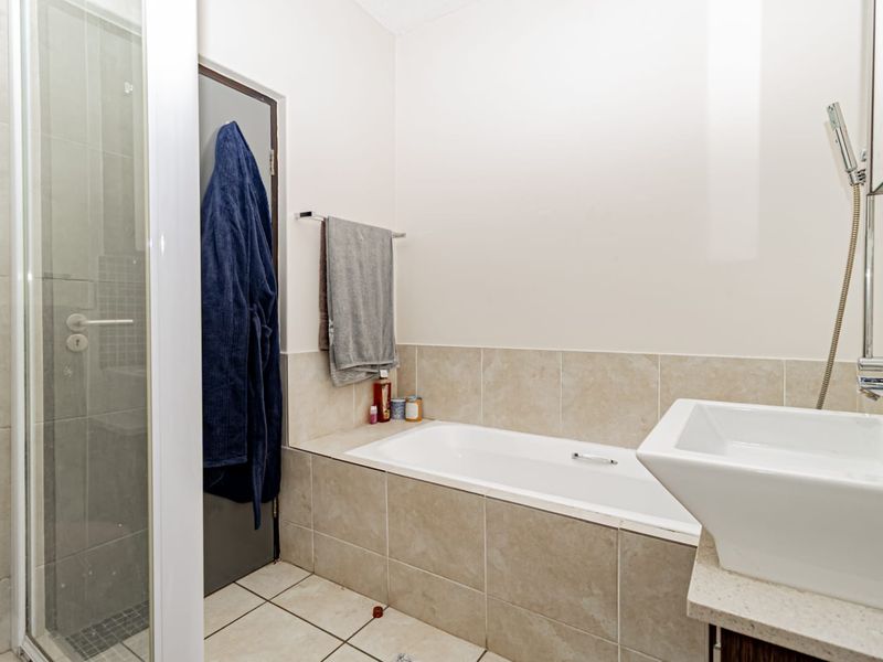 A functional bathroom featuring a tiled bathtub, separate shower enclosure, and a wall-mounted basin with neutral wall finishes.