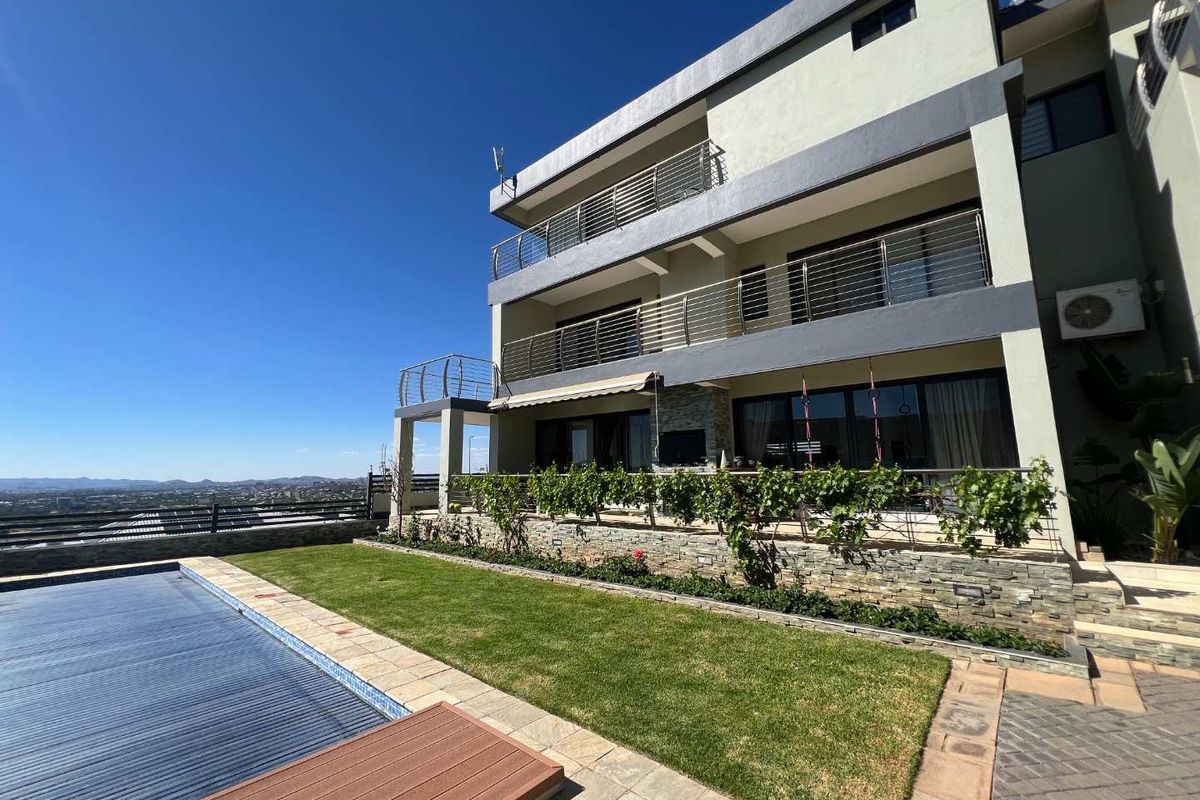 A multi-level rear exterior featuring a swimming pool with cover, landscaped garden, stone-clad retaining wall, and spacious balconies with stainless steel balustrades.