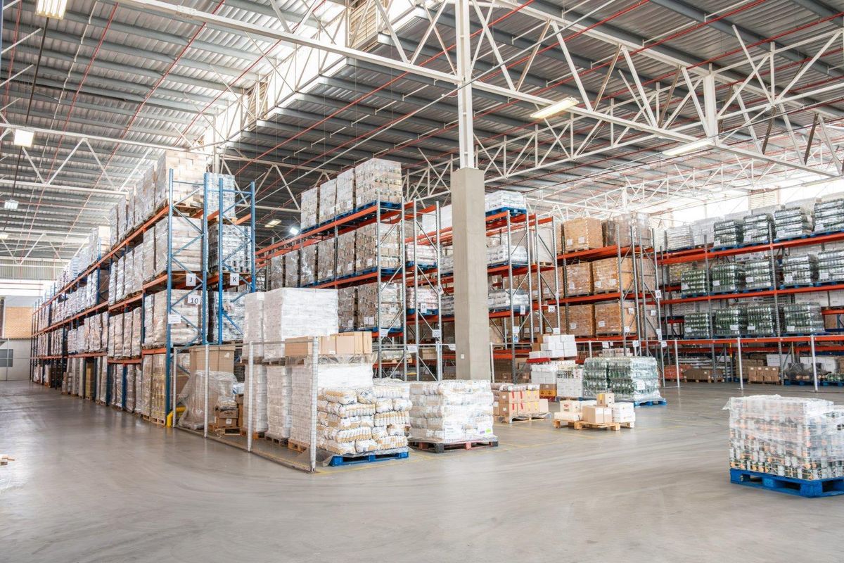 Spacious industrial warehouse facility featuring high-bay ceilings, exposed steel trusses, durable concrete flooring, and extensive integrated steel racking systems for storage.