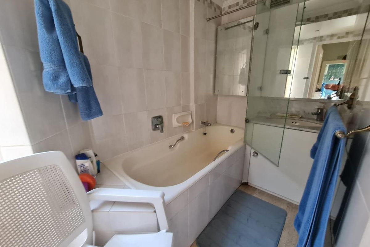 A functional bathroom featuring a built-in bathtub with shower mixer, glass shower screen, and vanity basin with integrated cabinetry.