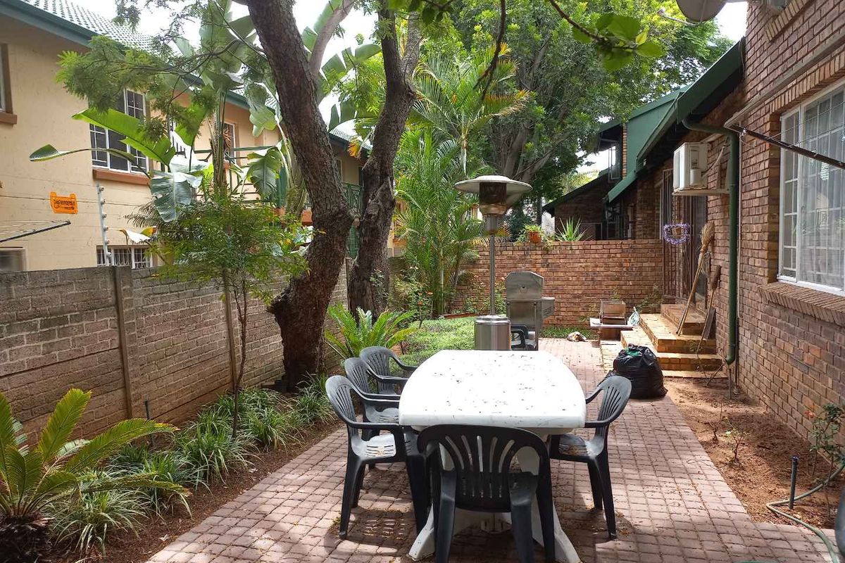 A private rear courtyard featuring brick paving, established trees, and a brick boundary wall, providing a functional outdoor space for the townhouse.