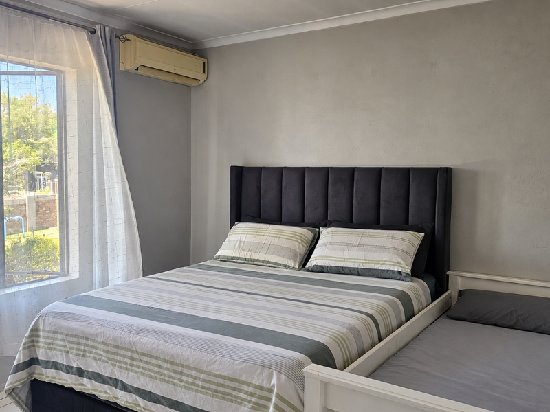A functional bedroom featuring tiled flooring and a wall-mounted air conditioning unit, offering a comfortable space with natural light.
