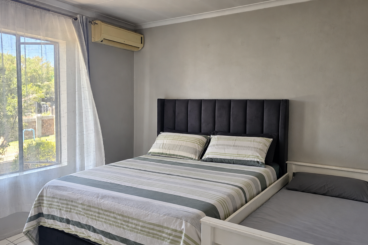A functional bedroom featuring tiled flooring and a wall-mounted air conditioning unit, offering a comfortable space with natural light.