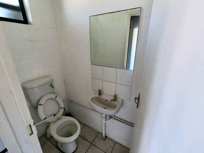 A compact industrial-style bathroom featuring a basic toilet, wall-mounted basin, and tiled flooring with exposed plumbing.