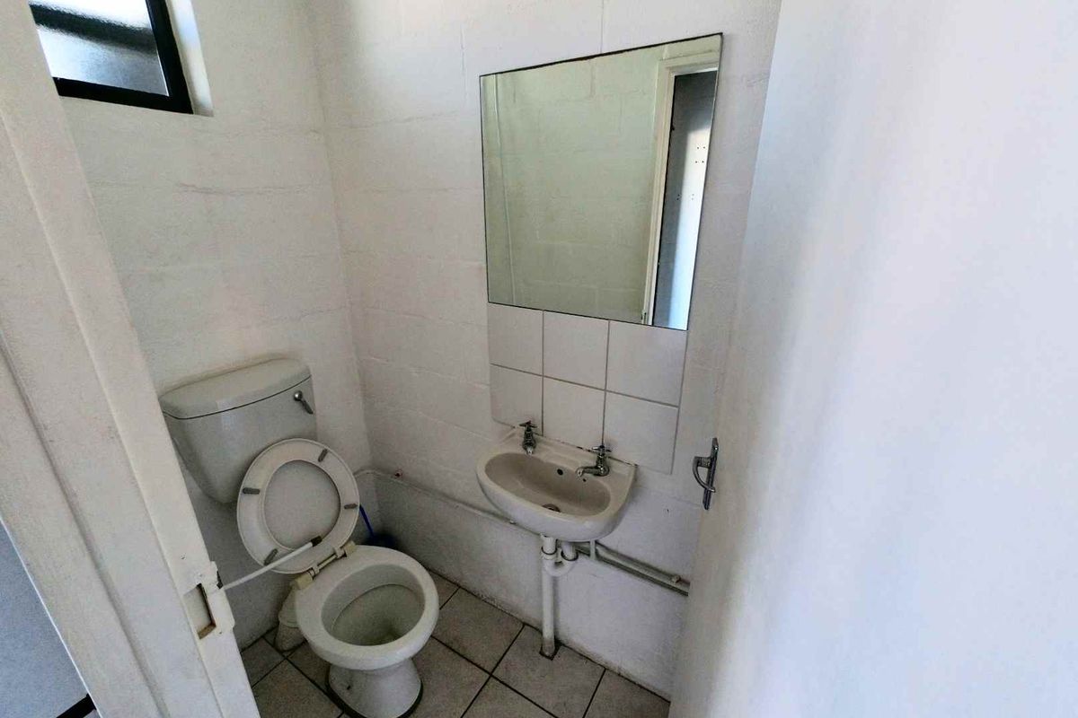 A compact industrial-style bathroom featuring a basic toilet, wall-mounted basin, and tiled flooring with exposed plumbing.