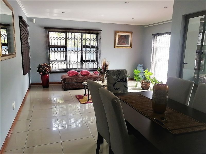 Spacious open-plan living and dining area featuring neutral tiled flooring, recessed downlighting, and large windows fitted with security bars and blinds.