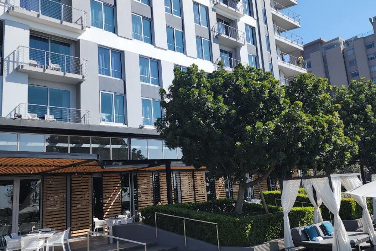 Exterior view of a modern apartment building featuring a landscaped terrace area with wooden decking, metal railings, and integrated outdoor seating spaces.