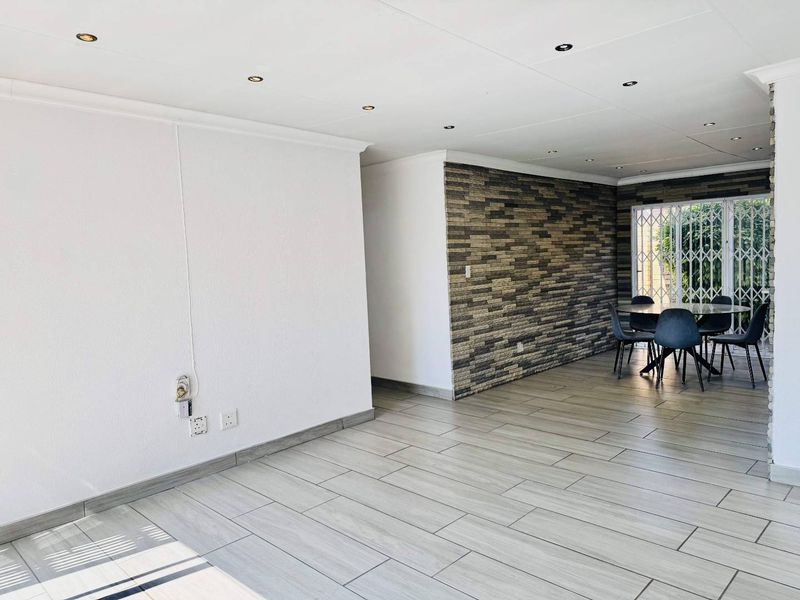 Spacious open-plan living area featuring modern wood-look ceramic floor tiles, a textured stone cladding feature wall, and recessed downlighting.