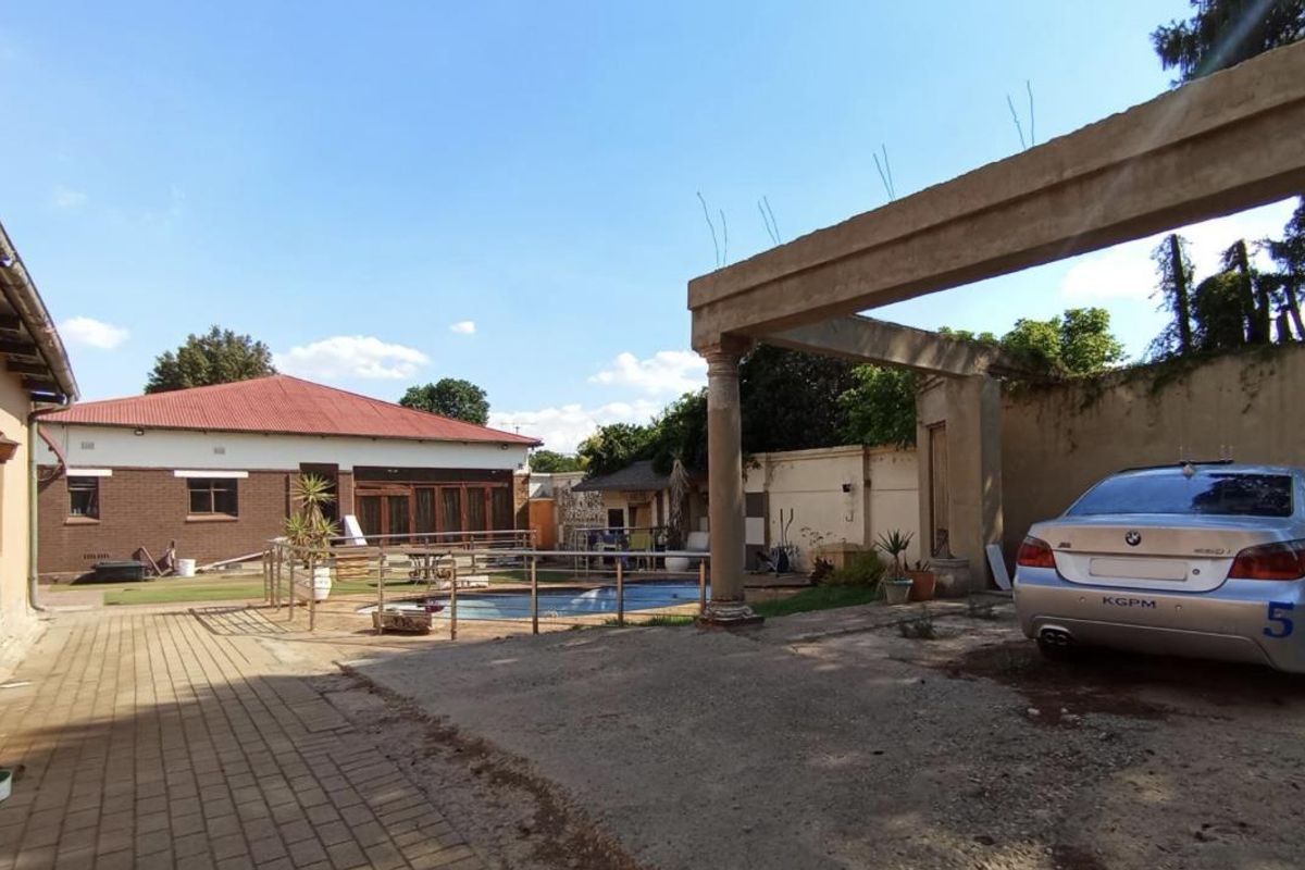 Rear exterior view featuring a swimming pool, paved courtyard, and an unfinished concrete pergola structure with exposed rebar.