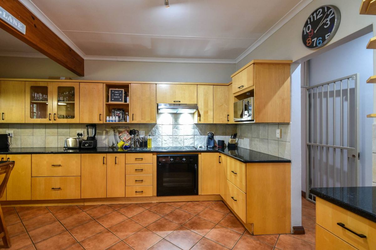 A functional kitchen featuring light wood cabinetry, black granite countertops, a built-in oven, extractor fan, and terracotta floor tiles.