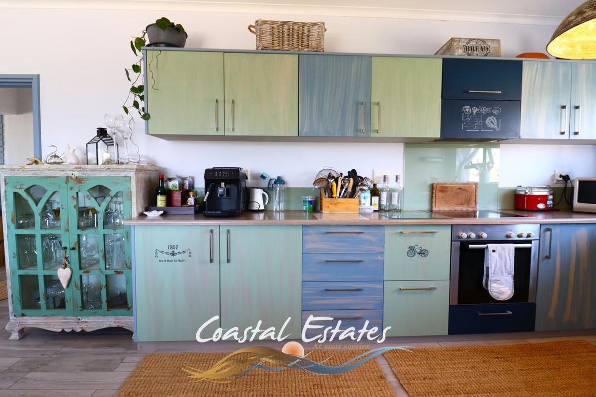 A kitchen featuring custom-painted cabinetry in blue and green tones, integrated oven, hob, and glass splashback.