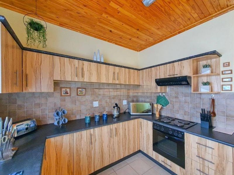 A functional kitchen featuring wood-look cabinetry, dark countertops, tiled backsplash, and a distinctive timber tongue and groove ceiling.