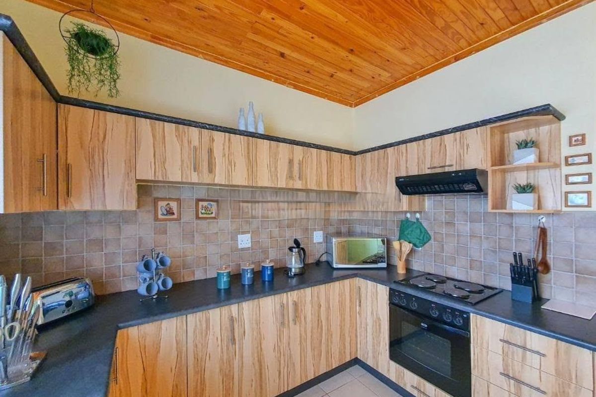 A functional kitchen featuring wood-look cabinetry, dark countertops, tiled backsplash, and a distinctive timber tongue and groove ceiling.