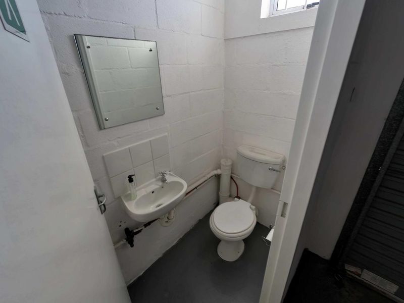A compact industrial-style restroom featuring a wall-mounted basin, toilet, and exposed plumbing with painted blockwork walls.