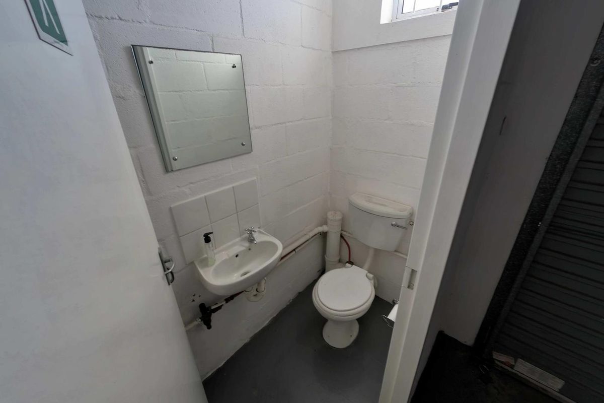 A compact industrial-style restroom featuring a wall-mounted basin, toilet, and exposed plumbing with painted blockwork walls.